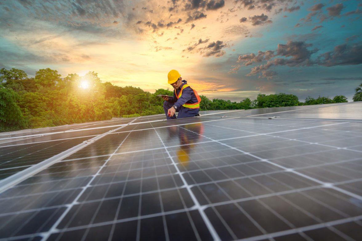 operaio con caschetto che sistema impianti fotovoltaici su un tetto al tramonto