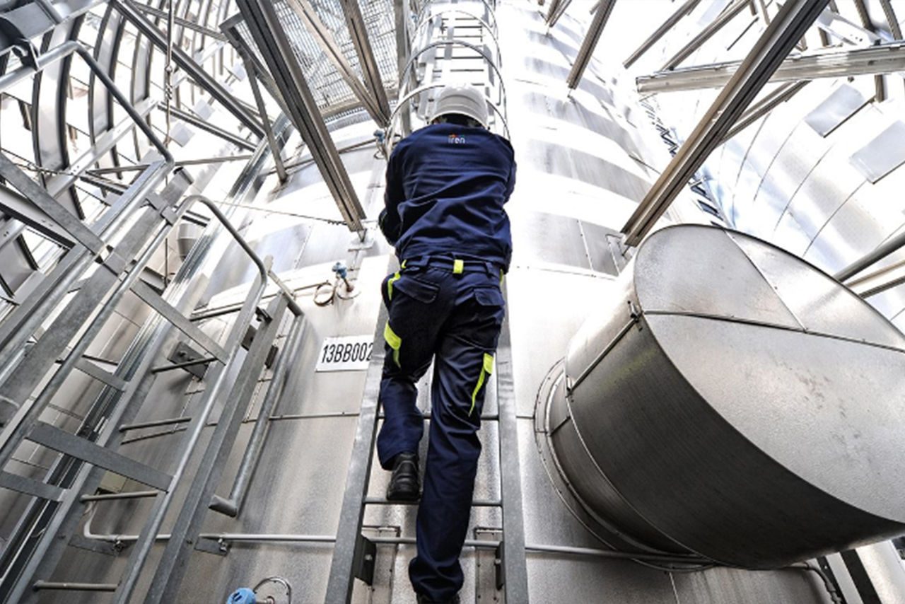 lavoratore con tuta blu e caschetto bianco che scale le scale di una cisterna