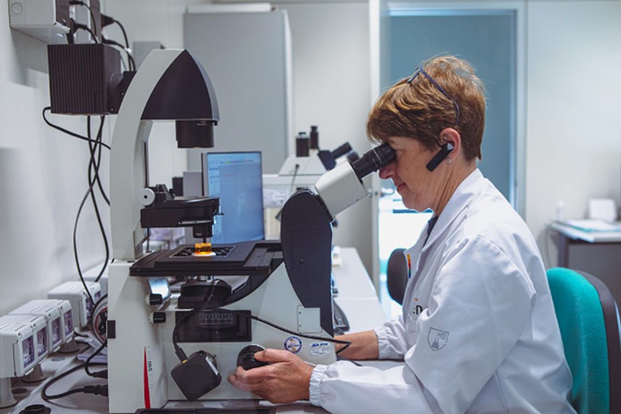 professionista con camice bianco e capelli corti, seduta a una scrivania, intenta a lavorare al microscopio