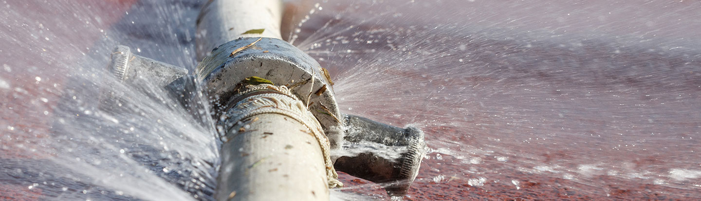 Primo piano di una perdita d’acqua da un foro in un tubo metallico, con gocce d’acqua che fuoriescono.