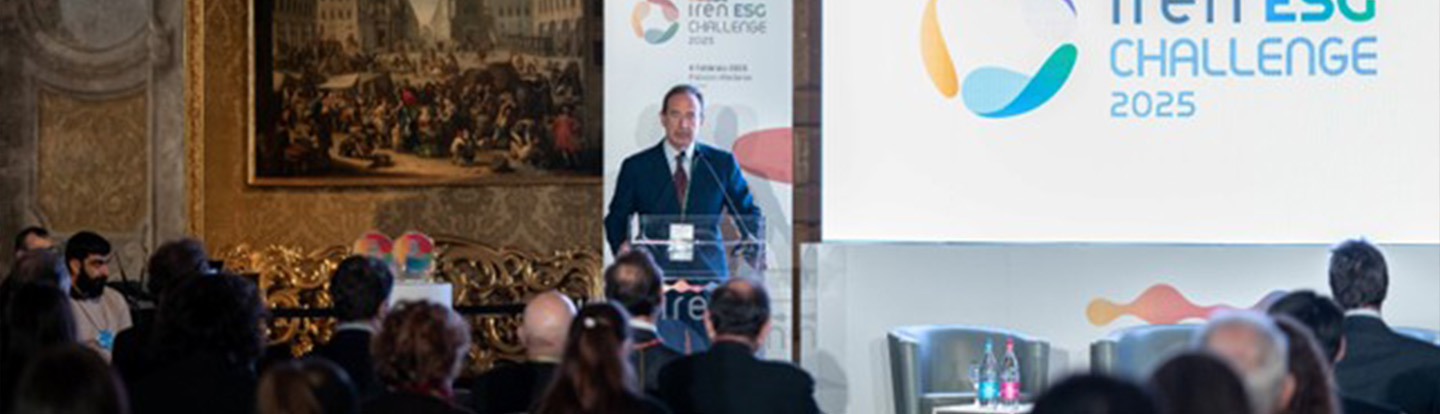 Luca Dal Fabbro in abito parla sul palco dell’Iren ESG Challenge 2025 di fronte a un pubblico attento. Sullo sfondo, uno schermo luminoso con il logo dell’evento e dettagli decorativi colorati.