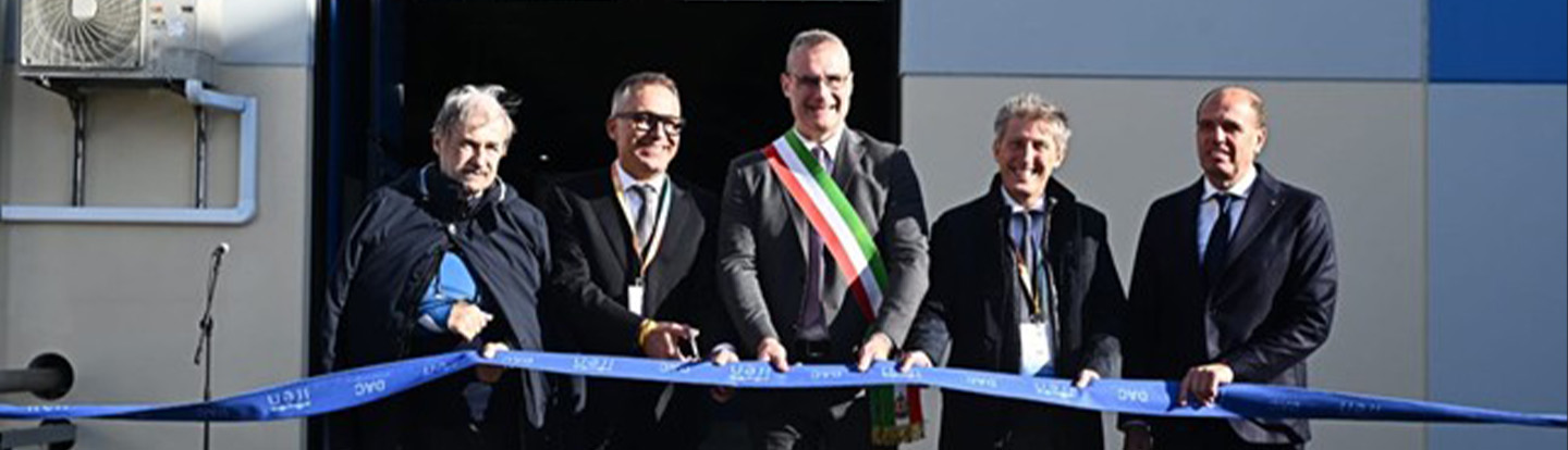 Cerimonia di inaugurazione con cinque uomini in abiti formali che tagliano un nastro blu davanti a un edificio con dettagli in blu e bianco.