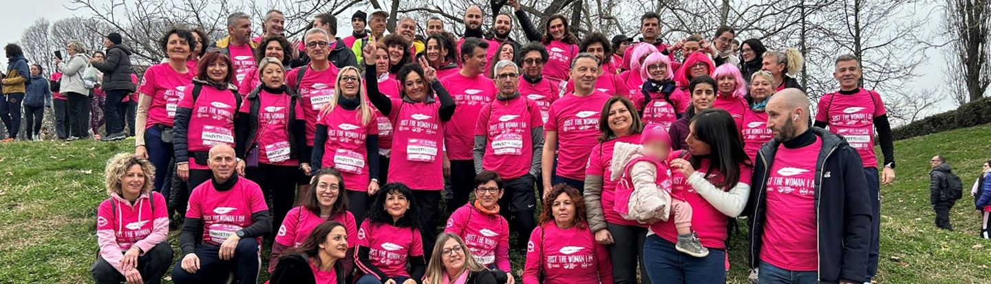 Partecipanti all'evento 'Just the Woman I Am' indossano magliette rosa mentre posano per una foto di gruppo su una collina, con un'atmosfera festosa e solidale.