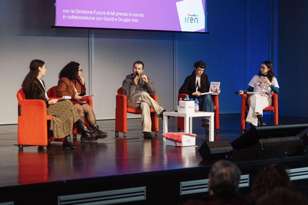 Panel di discussione sul palco con cinque partecipanti seduti su poltrone rosse, durante un evento promosso da Iren. Un uomo al centro parla con un microfono, mentre gli altri ascoltano o prendono appunti. Sullo sfondo, un grande schermo con il logo Iren e il titolo dell’incontro.