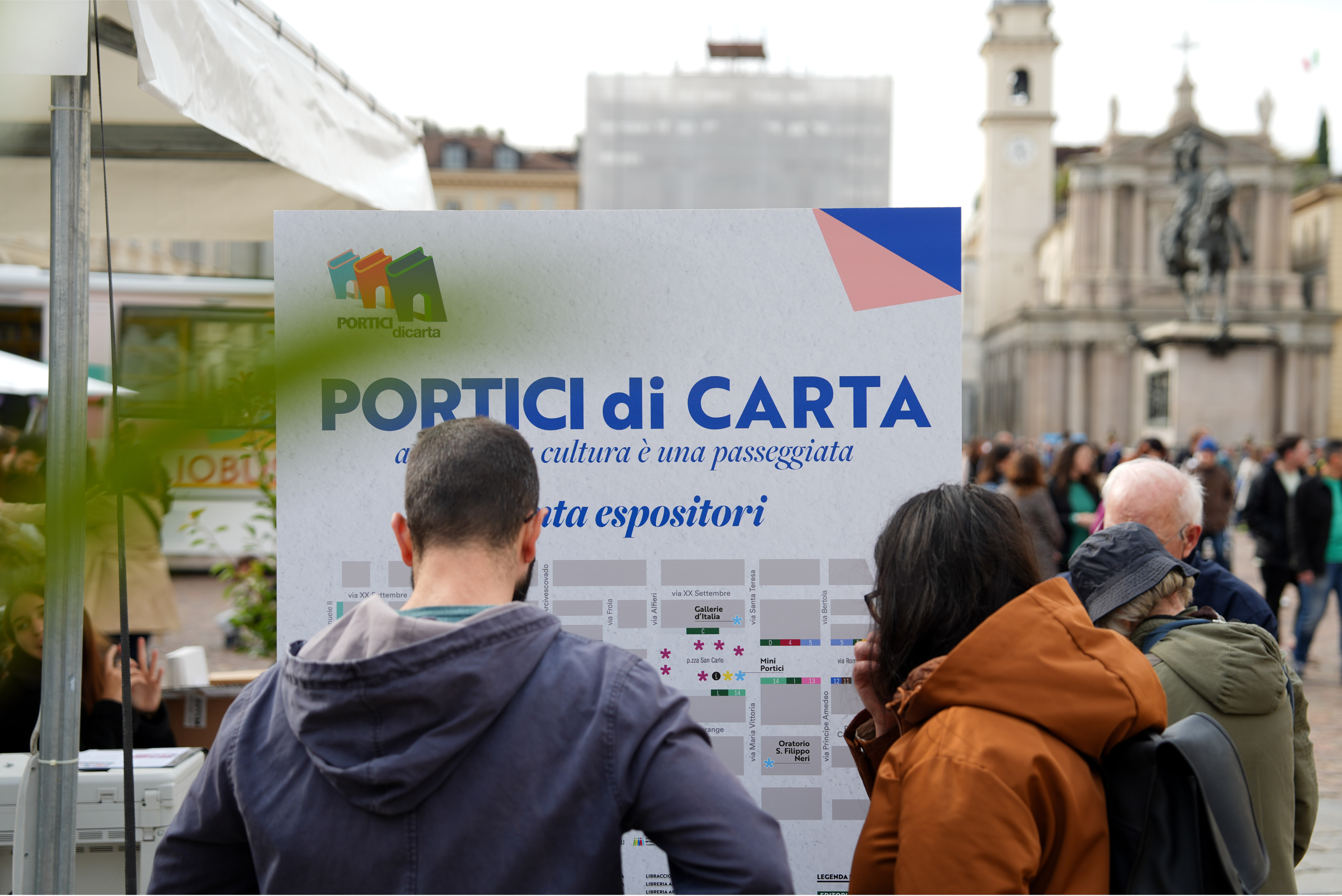 un ragazzo e una ragazza di spalle mentre leggono un manifesto dell'evento Portici di carta